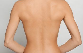 Back view of woman with perfect smooth skin on light grey background, closeup